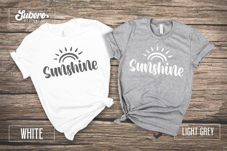 May include: Two t-shirts with the word "Sunshine" and a sun graphic. One t-shirt is white with a gray graphic and the other is light gray with a white graphic.
