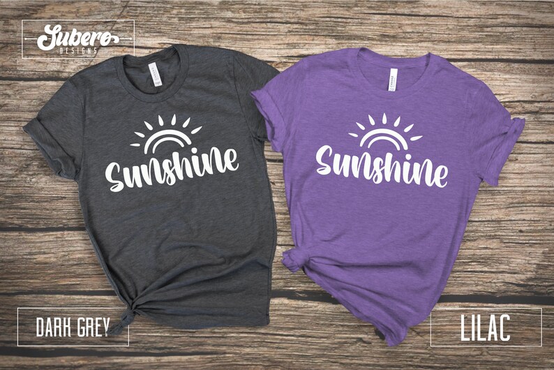 May include: Two t-shirts with the text "Sunshine" and a sun graphic. The shirt on the left is dark grey and the shirt on the right is lilac.