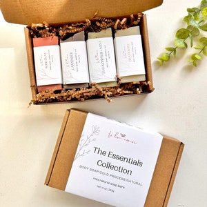 May include: A brown cardboard box set containing mini natural soap bars. The open box reveals four bars labeled Rose Clay, Lavender, Eucalyptus + Mint, and Chamomile. A second box is closed, with a white label reading "The Essentials Collection". The net weight is 10 oz.