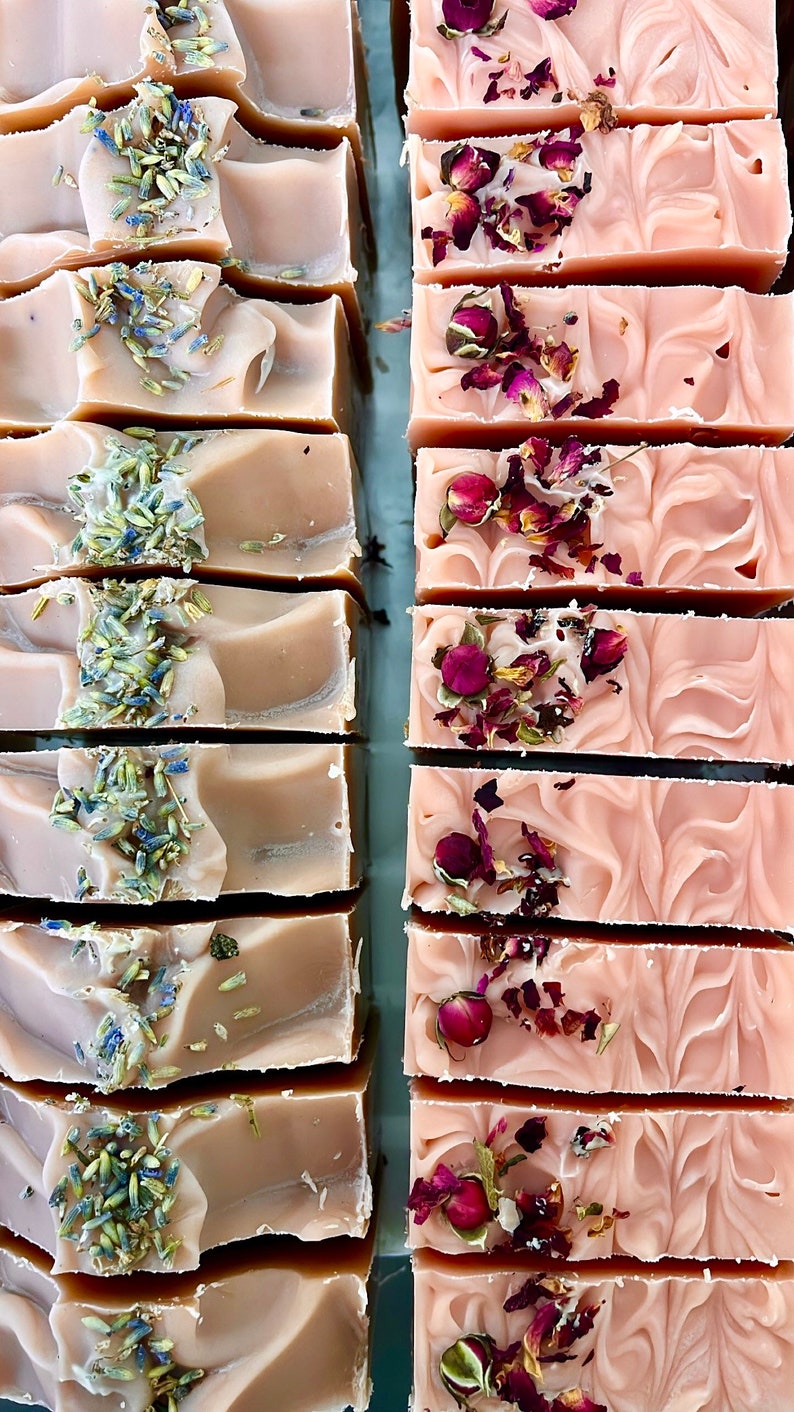 May include: Two rows of handmade soap bars. The top row features lavender-scented soap with dried lavender buds. The bottom row features rose-scented soap with dried rose petals.