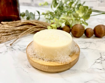 May include: A white soap bar with a foamy top, sitting on a wooden soap dish. The soap dish is made of bamboo and has a natural wood finish.