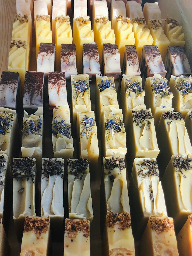 May include: A collection of handmade soap bars in various colors and patterns, including green, brown, and white. The bars are arranged in rows and columns, creating a visually appealing display.