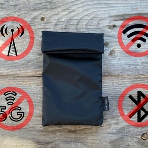 Può includere: Una pochette nera con una patta pieghevole e un'etichetta bianca con la scritta "Signal Blocker". La pochette è circondata da cerchi rossi con linee diagonali che attraversano vari simboli wireless, tra cui una torre di telefonia mobile, wifi, 5G e bluetooth.