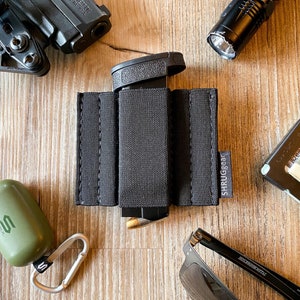 May include: A black fabric magazine holder with the text "SHRUGGEAR" printed on the side. The holder is designed to hold a magazine or other items securely.