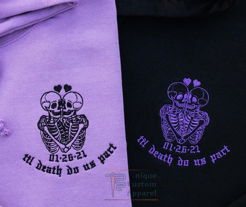 A close-up of two hoodies, one lavender and one black, showing the embroidered design of two skeletons embracing with a heart above their heads, and the text "til death do us part" and a date.