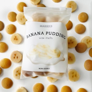 May include: A clear plastic bag filled with small, round, yellow wax melts shaped like banana slices. The bag is labeled "MARIEX3 BANANA PUDDING wax melts" and "NON-EDIBLE". The wax melts are surrounded by more of the same wax melts on a white surface.