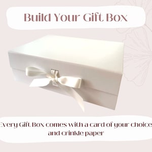 Könnte beinhalten: Eine weiße Geschenkbox mit einem Satinband und einem Kartensteckplatz. Der Text "Build Your Gift Box" befindet sich oben im Bild. Der Text "Every Gift Box comes with a card of your choice and crinkle paper" befindet sich unten im Bild.