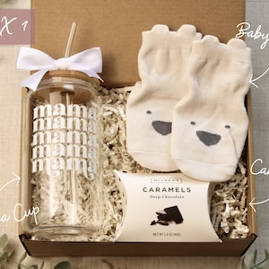 May include: A gift box filled with a glass cup with a straw, a package of caramels, and a pair of baby socks. The cup has the word "mama" printed on it multiple times. The box is labeled "BOX 1".