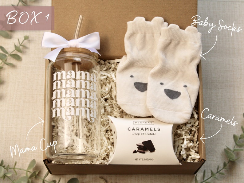 May include: A gift box filled with a glass cup with a straw, a package of caramels, and a pair of baby socks. The cup has the word "mama" printed on it multiple times. The box is labeled "BOX 1".