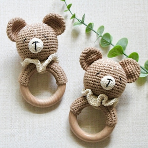 Puede incluir: Dos sonajeros de oso de crochet marrón con anillos de madera. Los osos tienen cuellos de crochet blanco y ojos y narices bordados en negro.