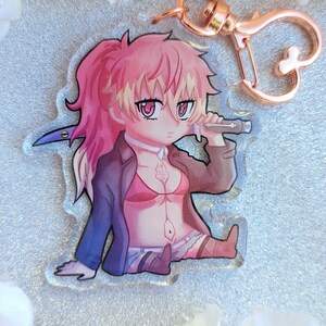 Peut inclure: Un personnage d'anime aux cheveux roses avec un microphone et une &eacute;p&eacute;e, tenant un microphone, dans un style chibi, sur un porte-cl&eacute;s en acrylique transparent.