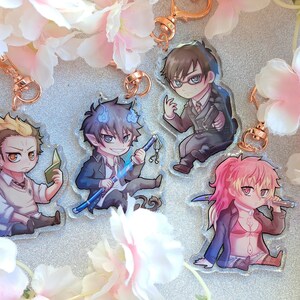 May include: Four anime character keychains with clear acrylic backgrounds. The characters are a blonde boy with a book, a blue-haired boy with a sword, a boy with brown hair and glasses, and a girl with pink hair and a knife.