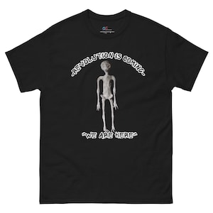 May include: Black t-shirt with a white graphic of a tall, thin, grey alien figure. The text "Revolution is coming" is above the alien and the text "We are here" is below the alien.