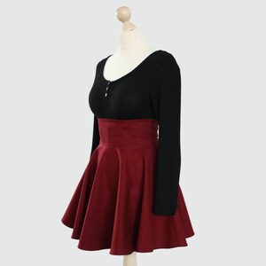 Puede incluir: Una falda de color burdeos de talle alto con silueta acampanada. La falda est&aacute; hecha de una tela suave y texturizada y tiene una cintura alta. La falda se combina con un su&eacute;ter negro de manga larga.