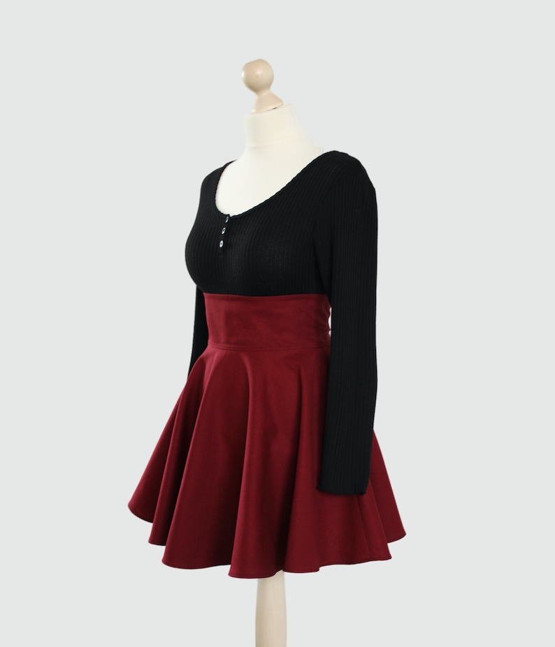 Puede incluir: Una falda de color burdeos de talle alto con silueta acampanada. La falda est&aacute; hecha de una tela suave y texturizada y tiene una cintura alta. La falda se combina con un su&eacute;ter negro de manga larga.