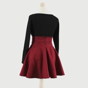 Puede incluir: Una falda de color burdeos de cintura alta con un jersey negro de manga larga. La falda tiene una silueta acampanada y una cremallera en la parte posterior.