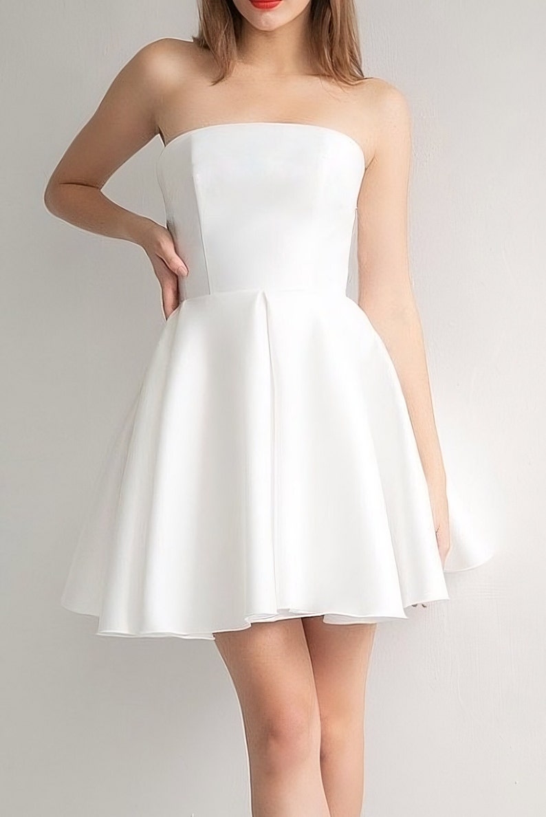 Puede incluir: Un vestido blanco sin tirantes con un corpi&ntilde;o ajustado y una falda completa y fluida. El vestido est&aacute; hecho de una tela lisa y satinada.