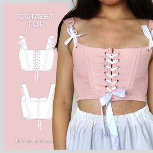 Pode incluir: Um top de corpete rosa com al&ccedil;as brancas e um cord&atilde;o branco na frente. O top tem um la&ccedil;o branco na parte inferior e o texto "CORSET TOP" est&aacute; impresso na imagem.