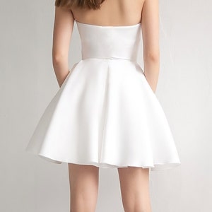 Puede incluir: Un vestido blanco sin tirantes, con un corpi&ntilde;o ajustado y una falda completa y fluida.