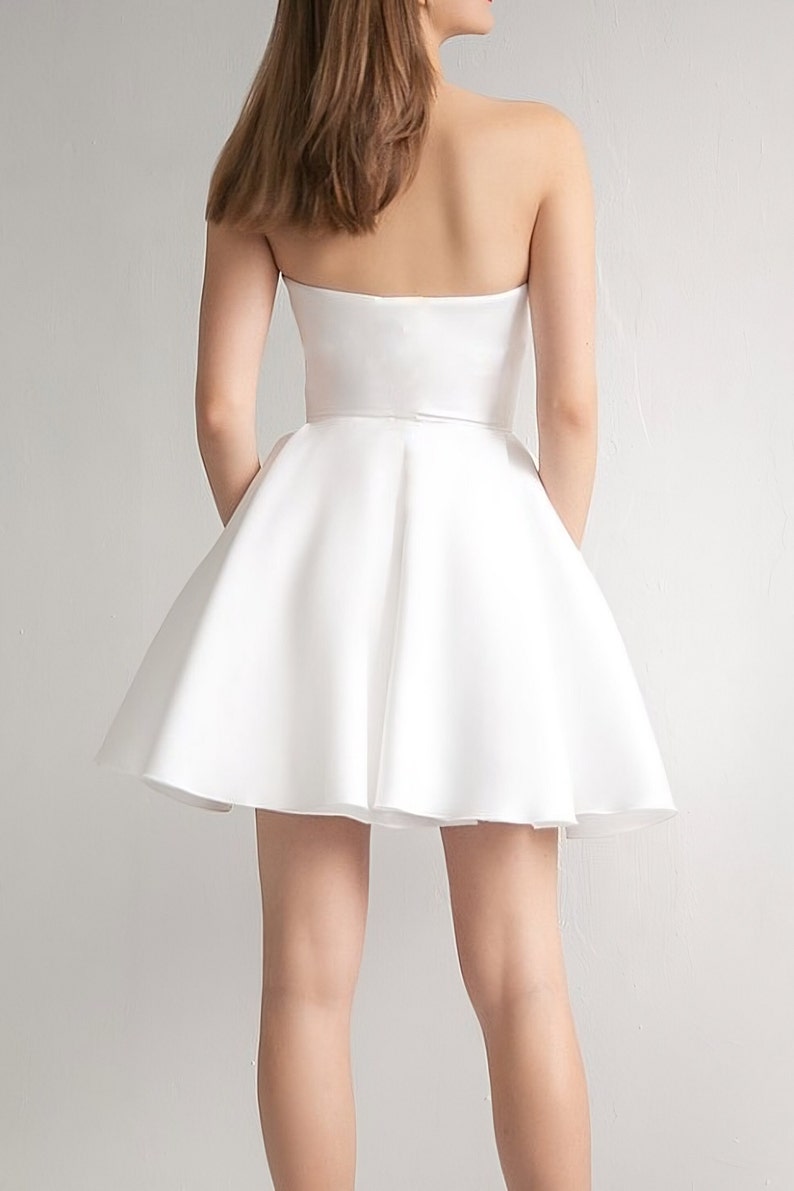 Puede incluir: Un vestido blanco sin tirantes, con un corpi&ntilde;o ajustado y una falda completa y fluida.