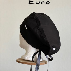 Puede incluir: Un gorro quir&uacute;rgico negro con lazo, exhibido en una cabeza de maniqu&iacute; blanca. El gorro tiene una peque&ntilde;a etiqueta blanca y la palabra "Euro" est&aacute; escrita en negro encima.