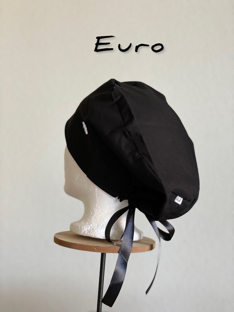 Puede incluir: Un gorro quir&uacute;rgico negro con lazo, exhibido en una cabeza de maniqu&iacute; blanca. El gorro tiene una peque&ntilde;a etiqueta blanca y la palabra "Euro" est&aacute; escrita en negro encima.