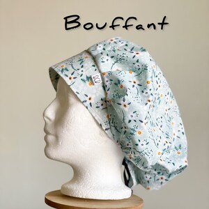 Puede incluir: Un gorro de quir&oacute;fano abombado azul claro con un estampado floral de flores blancas y amarillas y hojas verdes. La palabra "Bouffant" est&aacute; escrita en negro. El gorro se muestra en una cabeza de maniqu&iacute; blanca.