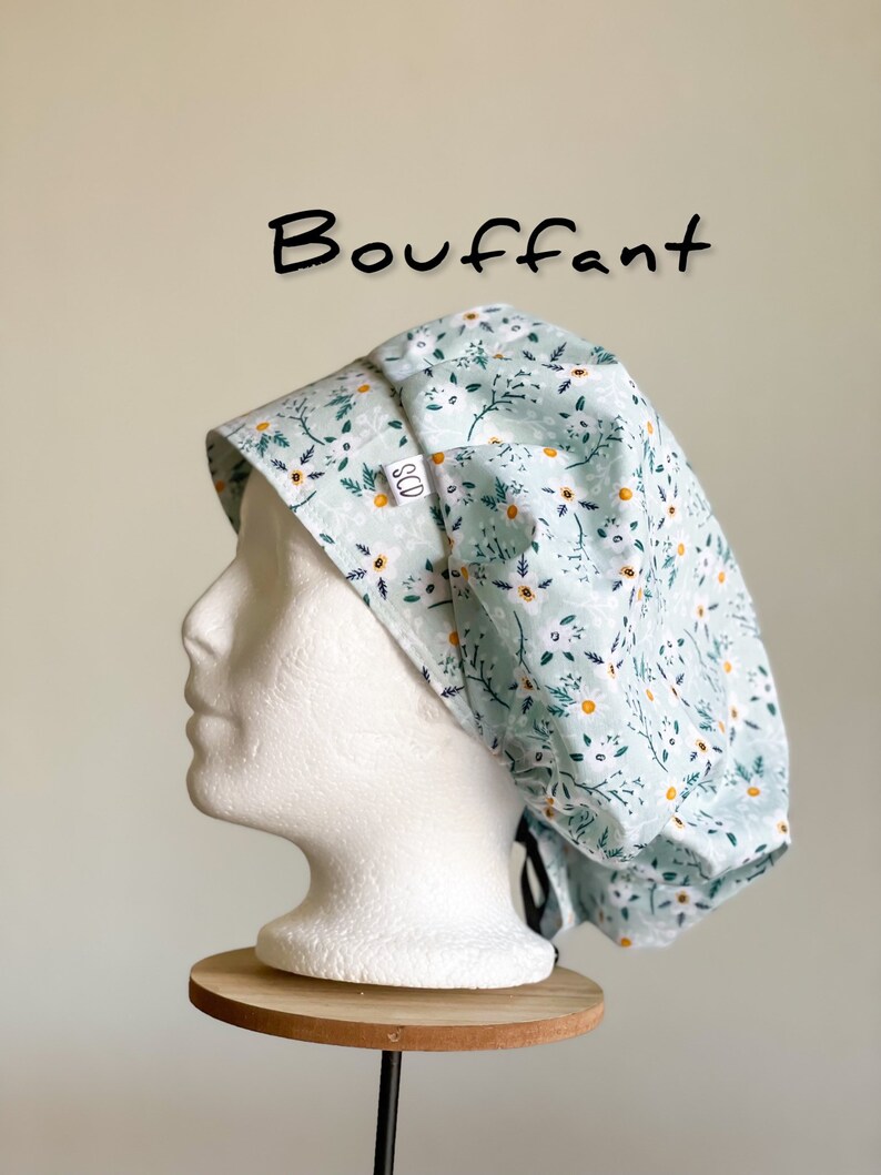 Puede incluir: Un gorro de quir&oacute;fano abombado azul claro con un estampado floral de flores blancas y amarillas y hojas verdes. La palabra "Bouffant" est&aacute; escrita en negro. El gorro se muestra en una cabeza de maniqu&iacute; blanca.