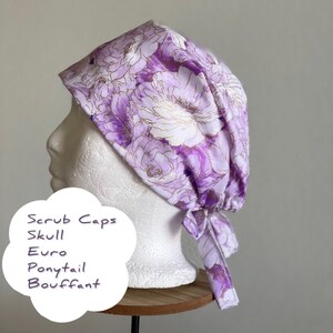Puede incluir: Un gorro quir&uacute;rgico floral en tonos morados y blancos, con detalles dorados. El gorro est&aacute; atado en la parte trasera y se muestra en una cabeza de maniqu&iacute;. El texto en la imagen dice: "Scrub Caps, Skull, Euro, Ponytail, Bouffant."