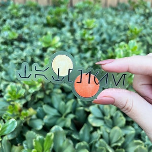 May include: Clear sticker with the word "SELVIG" written in black. The sticker has two circles, one yellow and one orange.