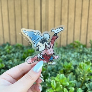 May include: A clear sticker featuring a cartoon image of Mickey Mouse dressed as a sorcerer, wearing a blue hat with stars and a red robe. The sticker has the text "aNickieMessofMagic" in the corner.