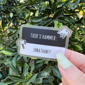May include: A gold sticker with a black background and white text that reads "Thor's Hammer: Jonathan??". A cartoon hammer with a smiley face and a cloud with lightning bolts are on the sticker.