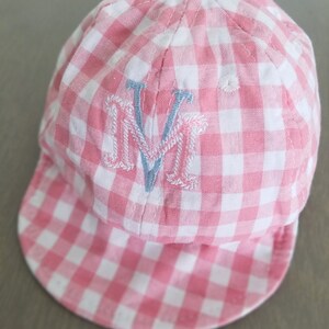 May include: Pink and white gingham baseball cap with a blue embroidered letter "M" on the front.
