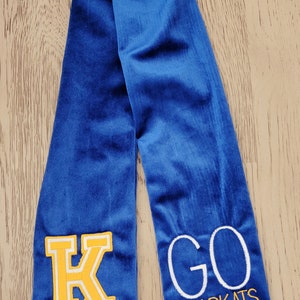 以下が含まれることがあります： 黄色のフェルトの文字「K」と白の刺繍で「GO BEARCATS」と刺繍された青い卒業式ストールです。