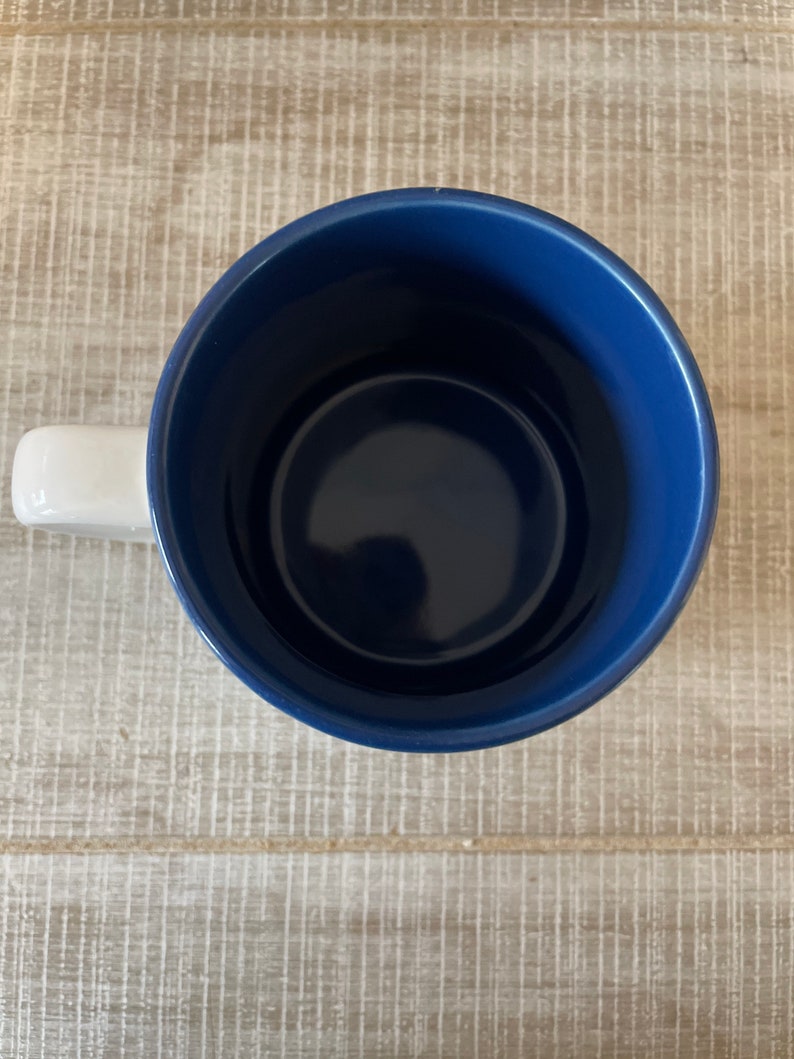 Puede incluir: Una taza de cer&aacute;mica azul con un asa blanca. La taza est&aacute; vac&iacute;a y el interior es visible.