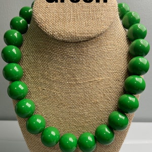 Puede incluir: Un collar de cuentas verdes con cuentas grandes y redondas. El collar se muestra en un maniquí de tela marrón.