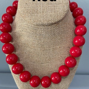 May include: A red beaded necklace with large, round beads. The necklace is displayed on a fabric-covered mannequin.