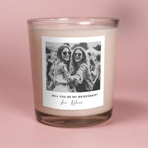 May include: A white candle with a black and white photo of two women smiling and the text "Will you be my bridesmaid? Love, Olivia" on the label.