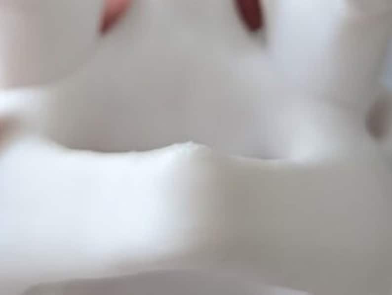 May include: Close-up of a white ceramic planter with a smooth, rounded rim. The planter has a slightly textured surface and a small opening at the bottom for drainage.