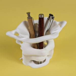 May include: White 3D printed pen holder shaped like a vertebrae, with three pens inside: a brown wooden pen, a dark red pen, and a silver pen.