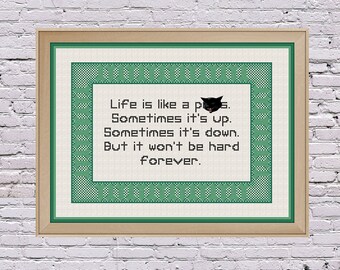 May include: A framed green and white cross-stitch with a black cat and the text "Life is like a puss. Sometimes it's up. Sometimes it's down. But it won't be hard forever."