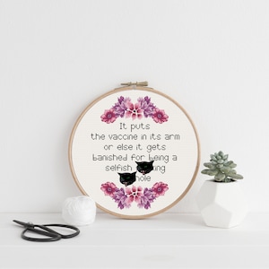 Può includere: Arte ricamata su un cerchio con fiori rosa e viola. Il testo recita "It puts the vaccine in its arm or else it gets banished for being a selfish king hole".
