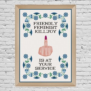 May include: A framed cross-stitch design with blue flowers and green leaves around the edges. The text reads "Friendly Feminist Killjoy is at your service" with a middle finger in the centre.