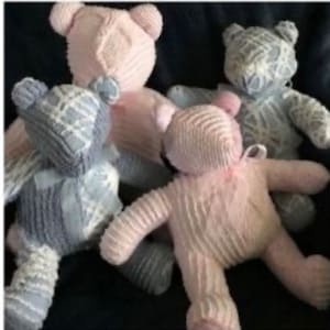 May include: Four handmade teddy bears in soft pastel colors. Two are pink, one is blue, and one is gray. The bears have a textured, knitted appearance and are arranged together. Each bear has a bow tied around its neck.