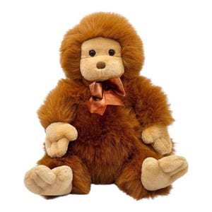 May include: A plush brown orangutan stuffed animal with a light brown face, hands, and feet. The stuffed animal has a brown bow around its neck and is sitting upright. The fur is soft and fluffy, and the toy has a friendly expression.