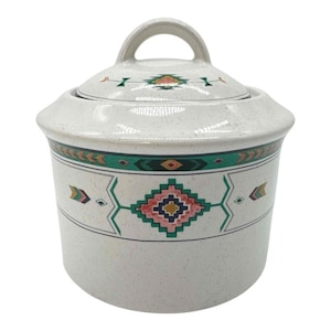 May include: A ceramic canister with a lid featuring a speckled off-white finish and a geometric pattern in teal, pink, and dark blue. The design includes a central diamond motif and horizontal bands encircling the body and the lid handle.
