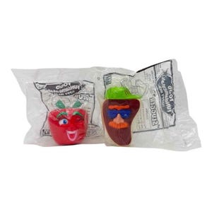 Può includere: Due giocattoli sigillati di McDonald's Happy Meal. Uno è una mela rossa con un volto sorridente e foglie verdi. L'altro è un peperone rosso con un volto, occhiali da sole e un cappello verde. Entrambi sono in confezioni di plastica trasparente.
