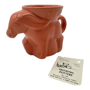 May include: A terracotta-coloured ceramic donkey mug with a handle. The mug is part of a collector series of elephant and donkey mugs from Frankoma Pottery.