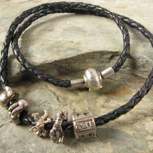 May include: A black leather bracelet with silver charms, including a charm with the word "family" engraved on it.