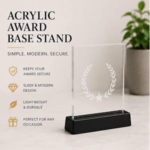 May include: Clear acrylic award base stand with a black base. The stand features a laurel wreath design and the text "ACRYLIC AWARD BASE STAND". The design is simple, modern, and secure.